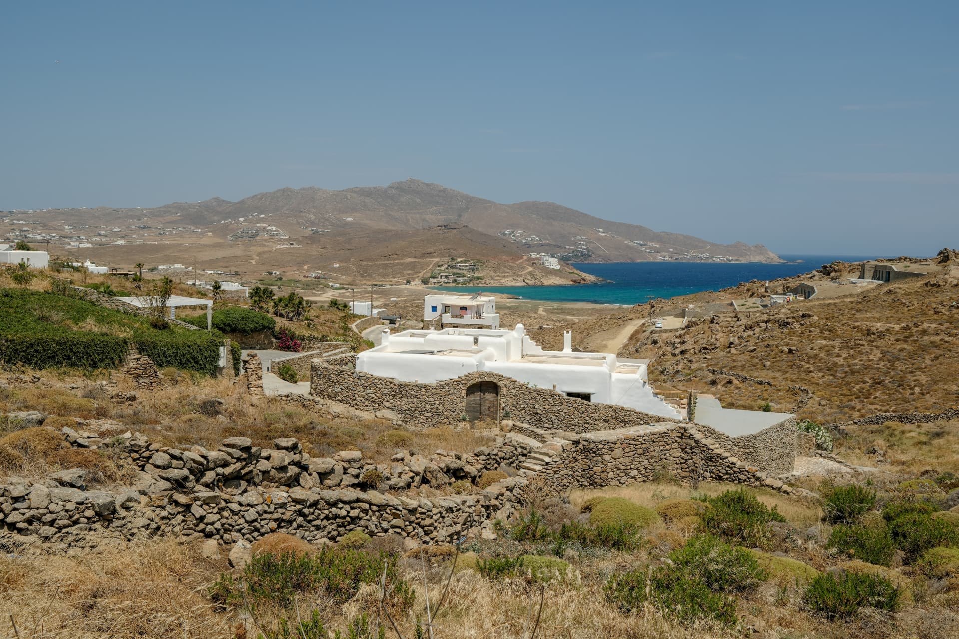 The villa's white building and low stone walls overlooking a blue bay and distant mountains