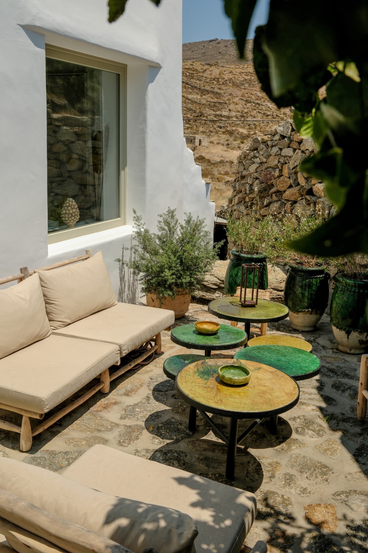 Patio at Villa Storia: wooden sofa with cream cushions, round glazed ceramic tables and large green pots against a stone wall