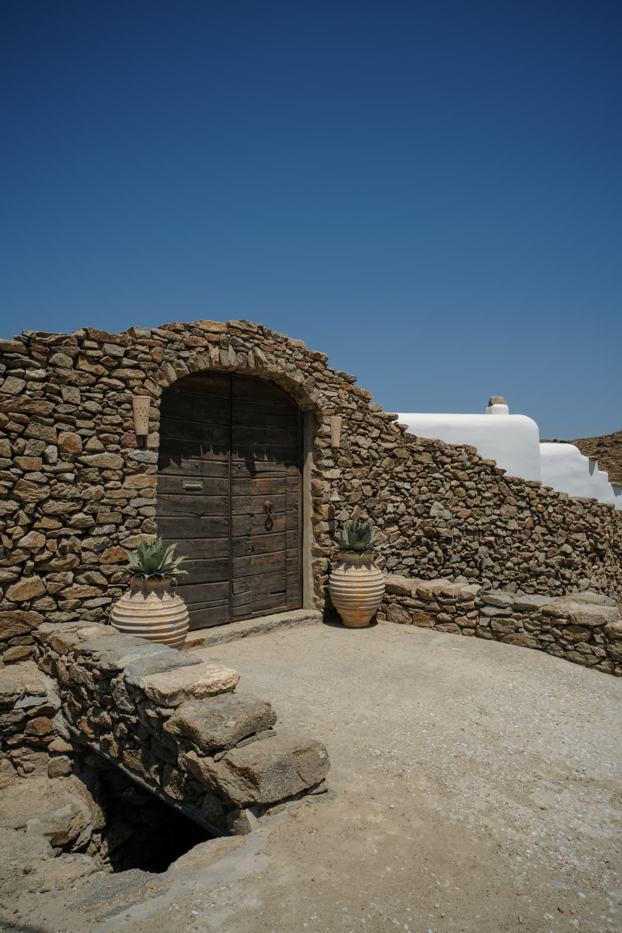 An old wooden door set into the stone architecture of the house, framed by terracotta pots and agave