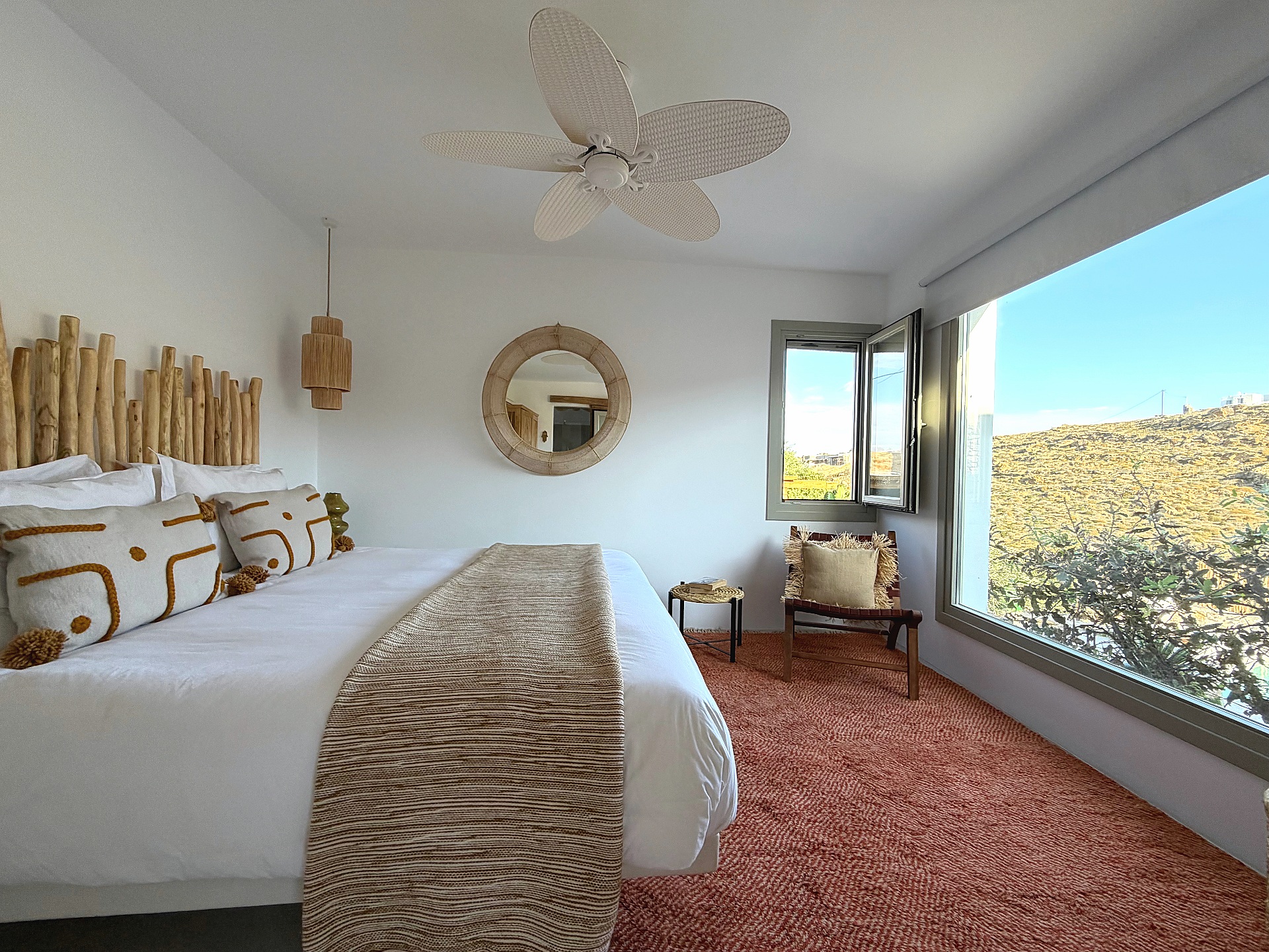 The Cycladic Suite bedroom bathed in natural light, picture window over the hills