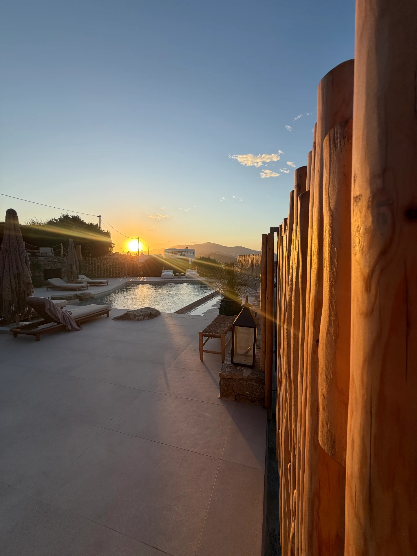 The sun setting over the poolside patio at Villa Storia, golden rays across a stone deck and a rustic wooden fence