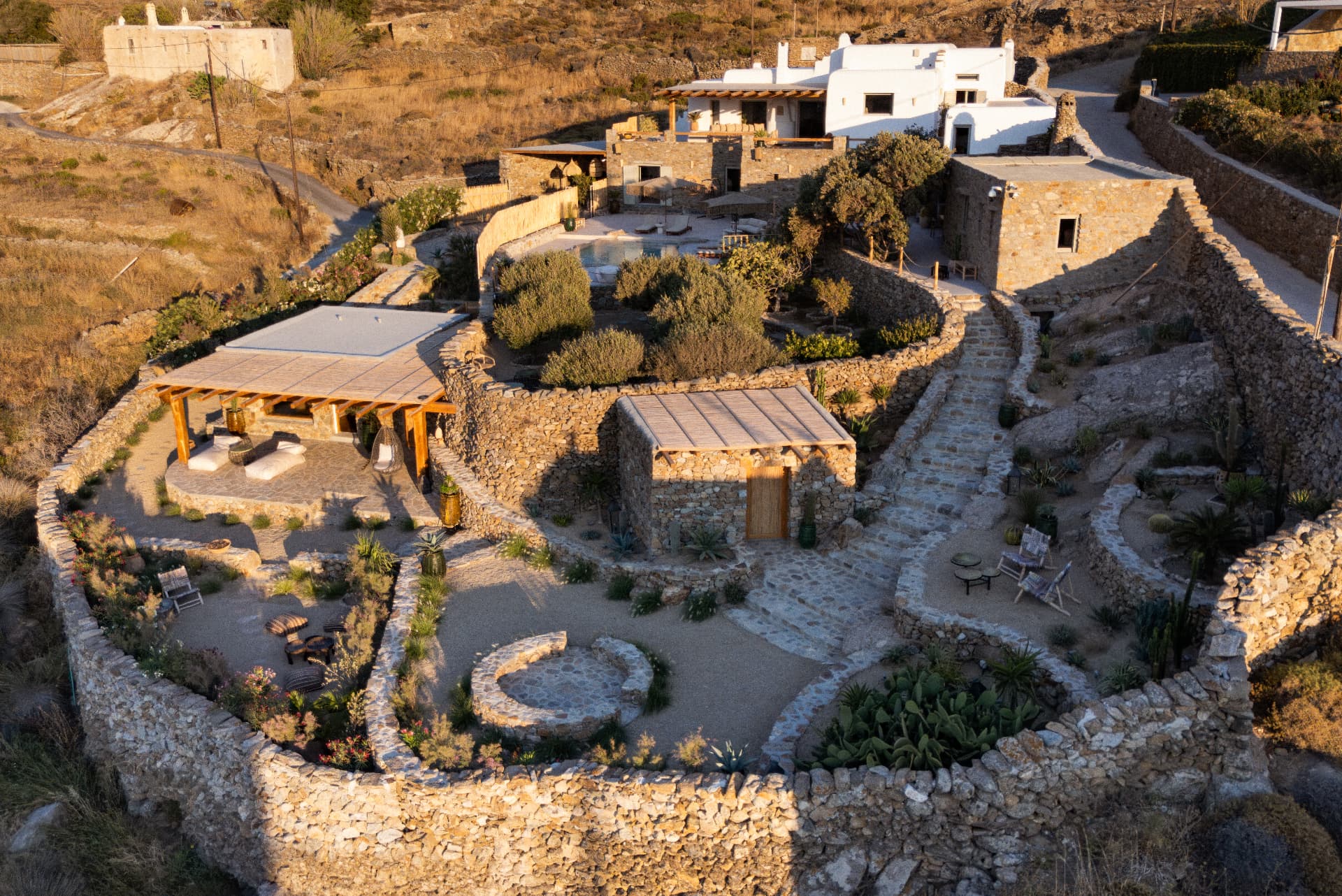 Aerial view of Villa Storia: terraced stone and white-plastered buildings, pool and pergola at golden hour