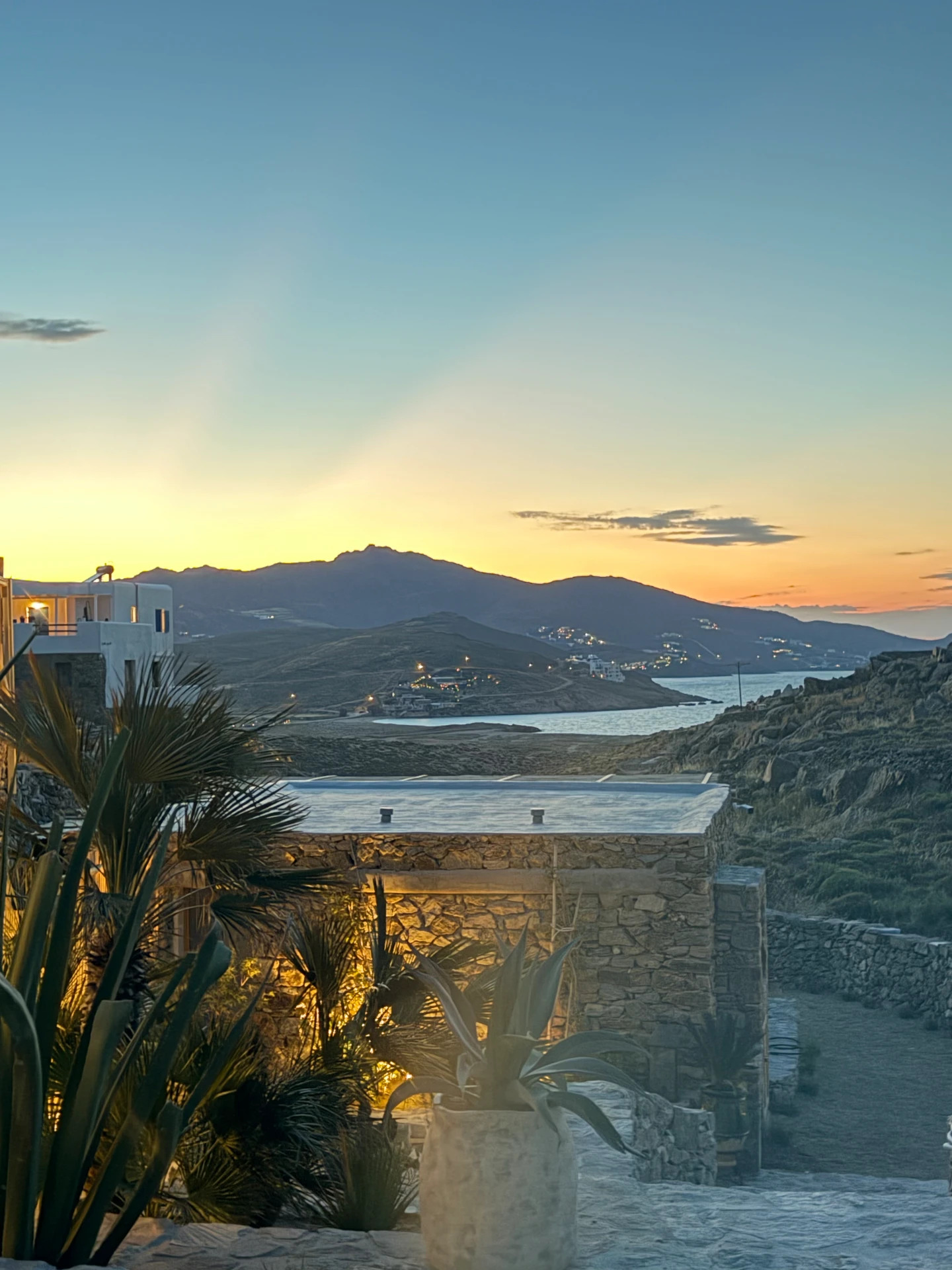 A soft twilight glow over the stone architecture and greenery of Villa Storia, with a quiet bay and distant mountains