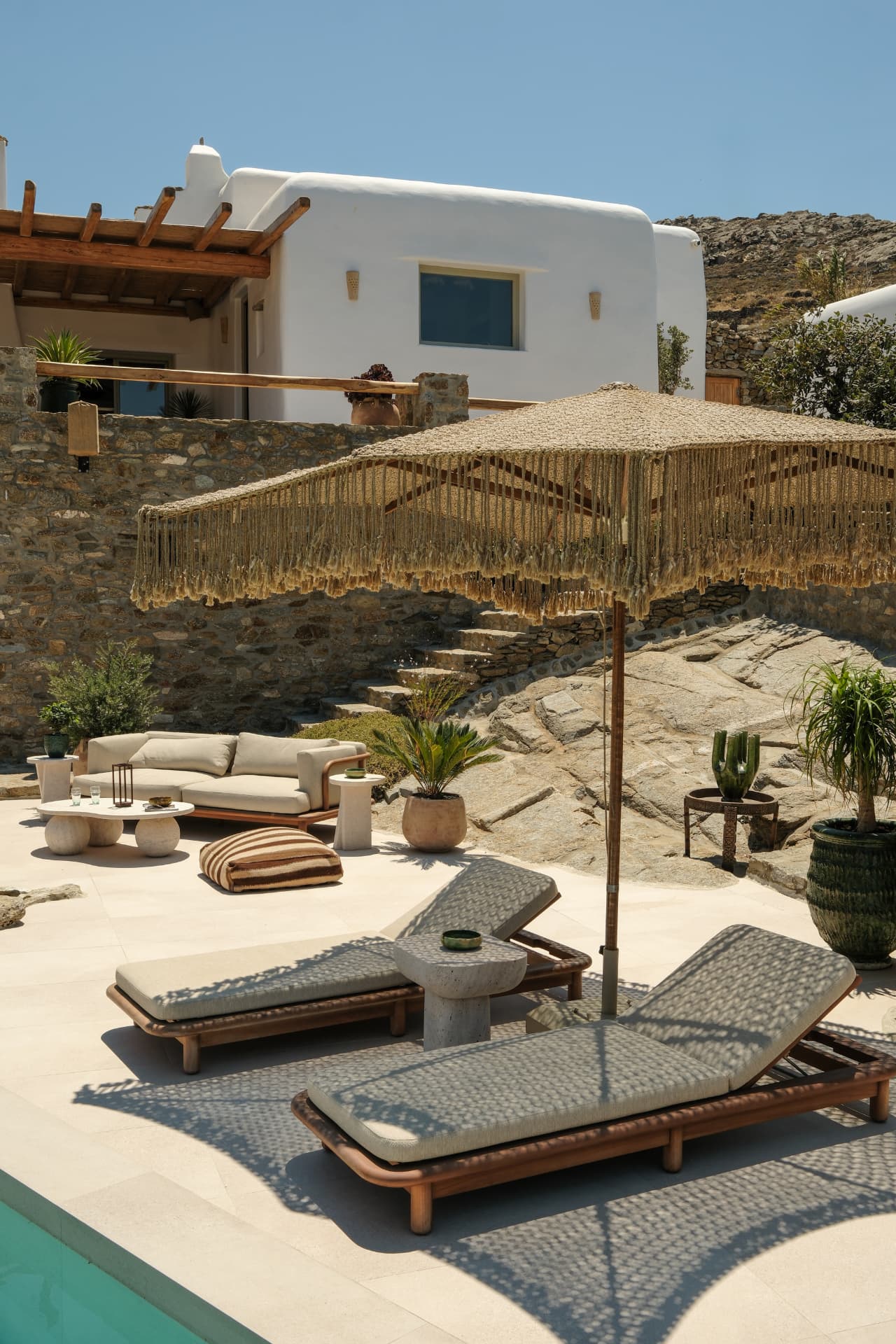 Sun loungers and a beige sofa on the stone terrace beside the pool