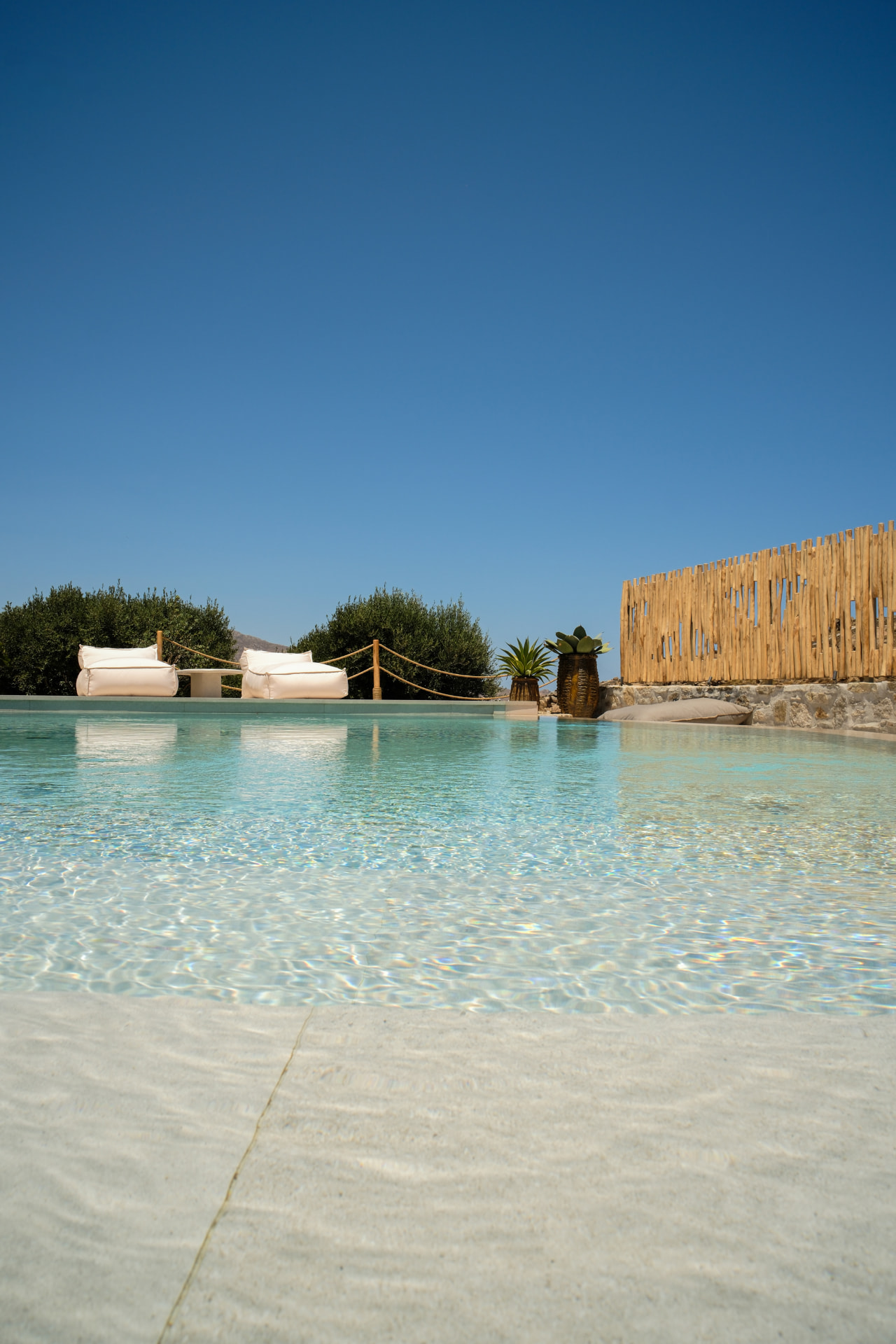 Water-level view of the pool, beanbag loungers and a rustic fence under a clear sky