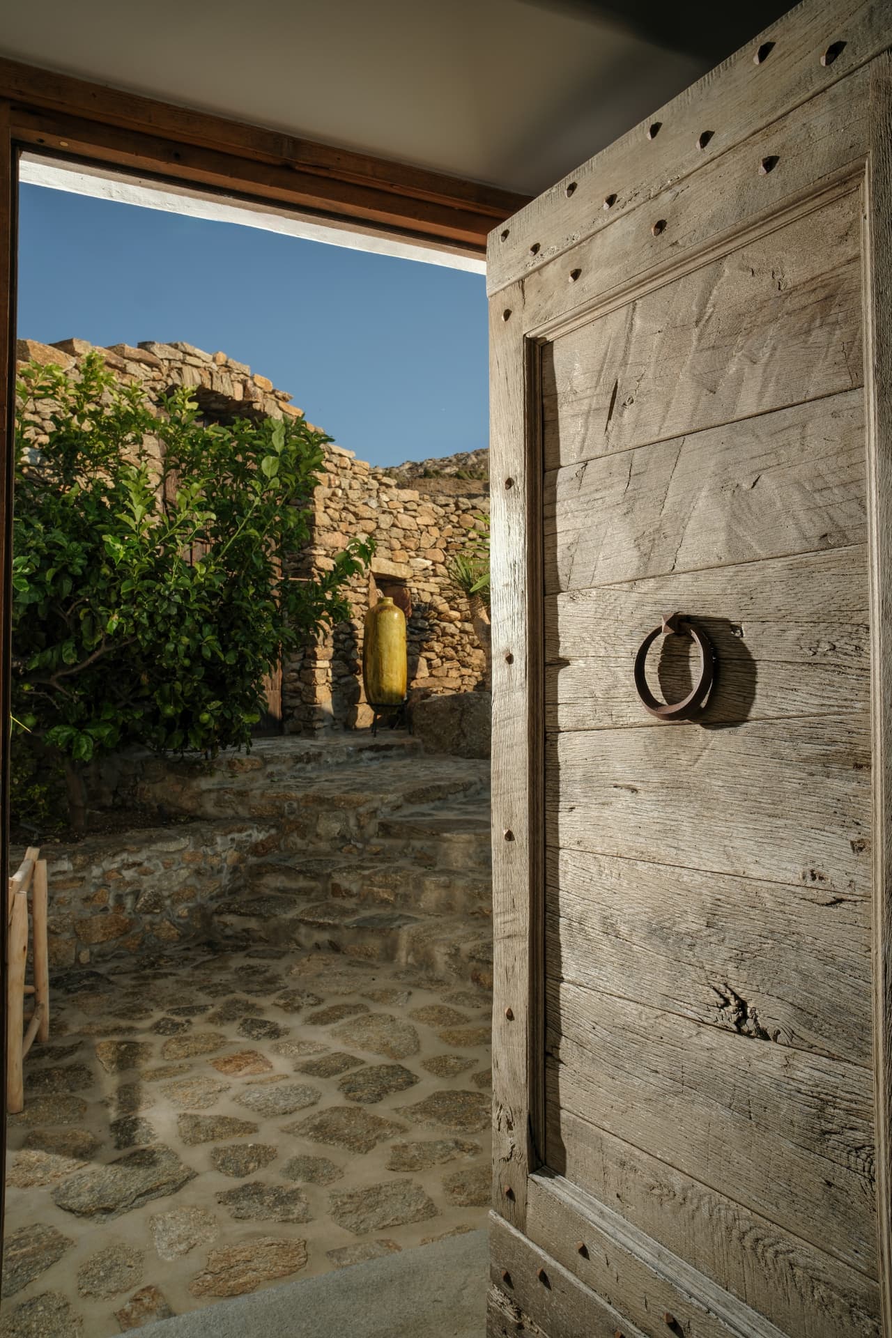 Detail, an open weathered wooden door opening onto a sunlit stone courtyard