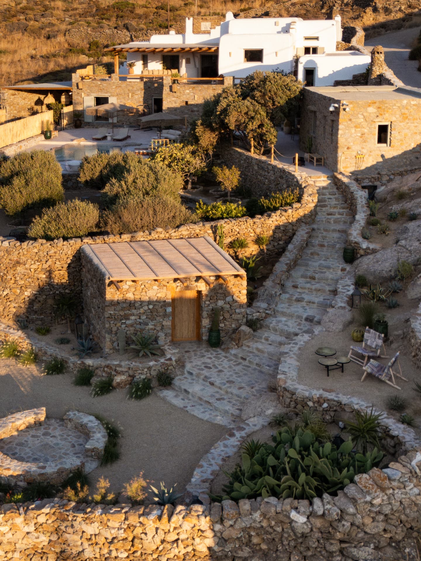 An aerial view of Villa Storia: stone and white-plastered buildings linked by paths at golden hour