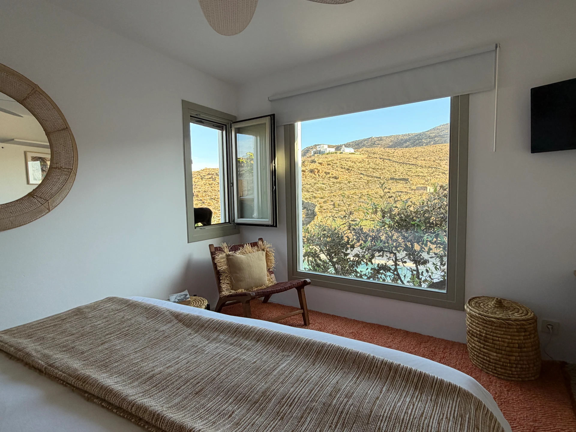 The Cycladic Suite bedroom, round mirror and window framing the hillside