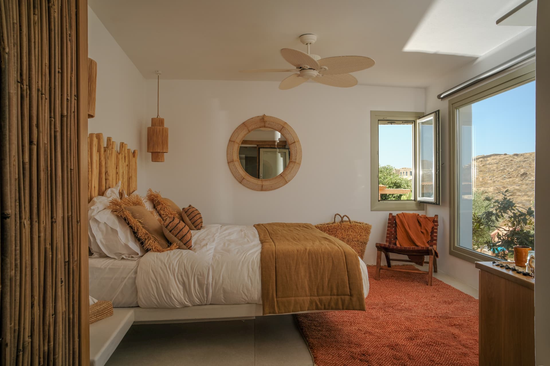The Cycladic Suite bedroom, sunlit bed with branch headboard and round mirror