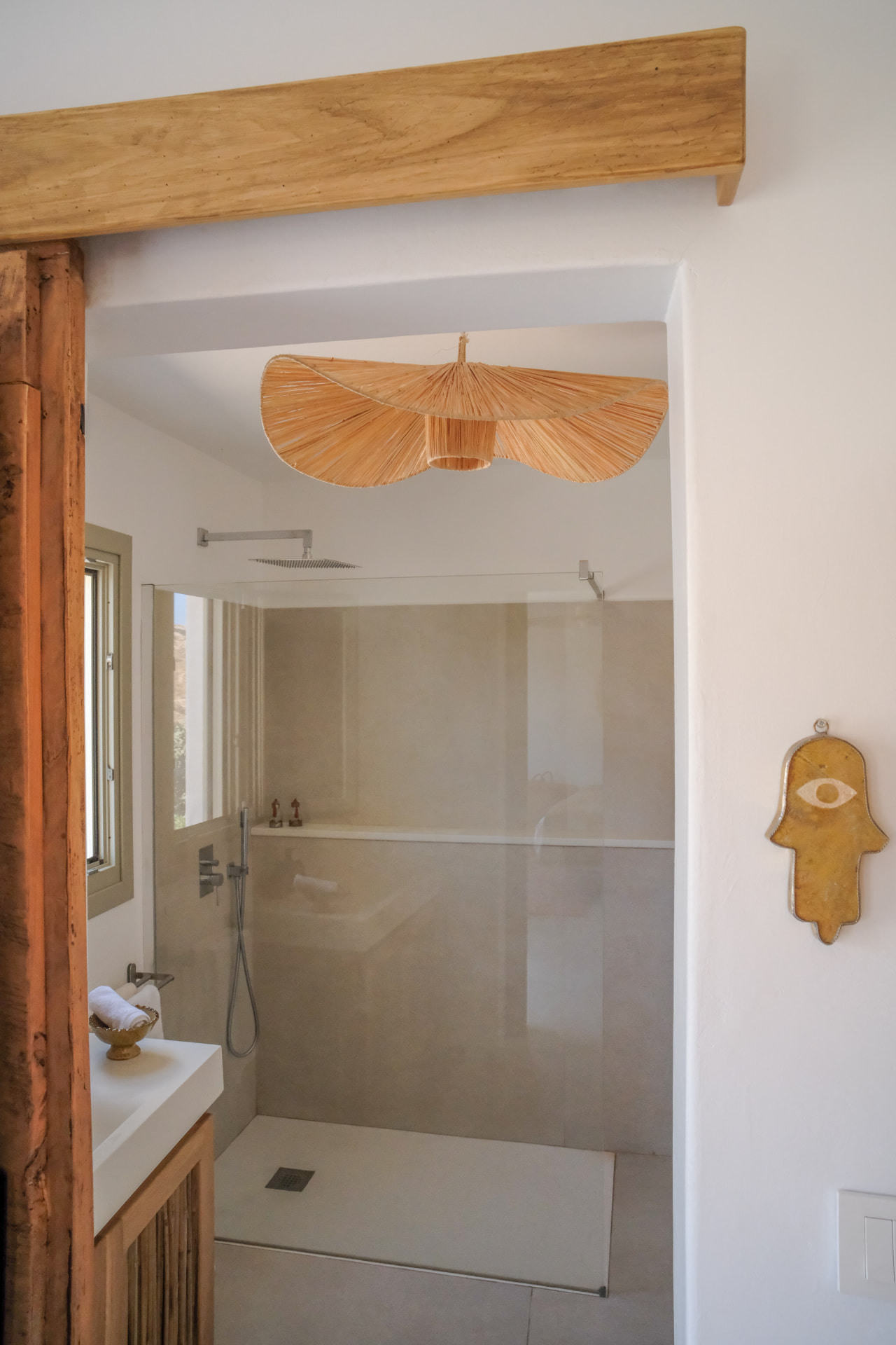 The Cycladic Suite bathroom seen through the wooden doorway, raffia pendant