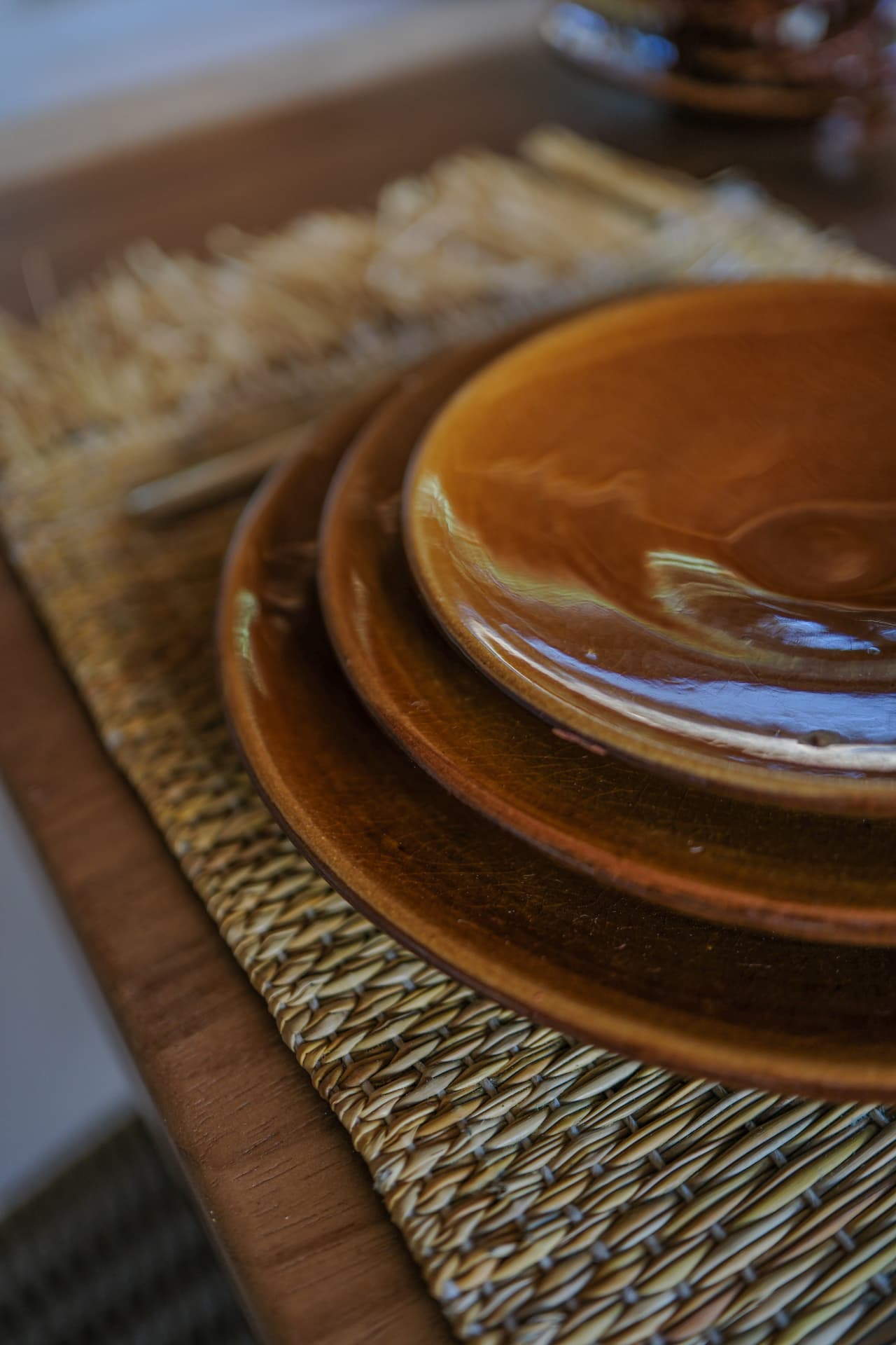 A stack of glossy earthy-brown ceramic plates on a woven placemat in warm natural light