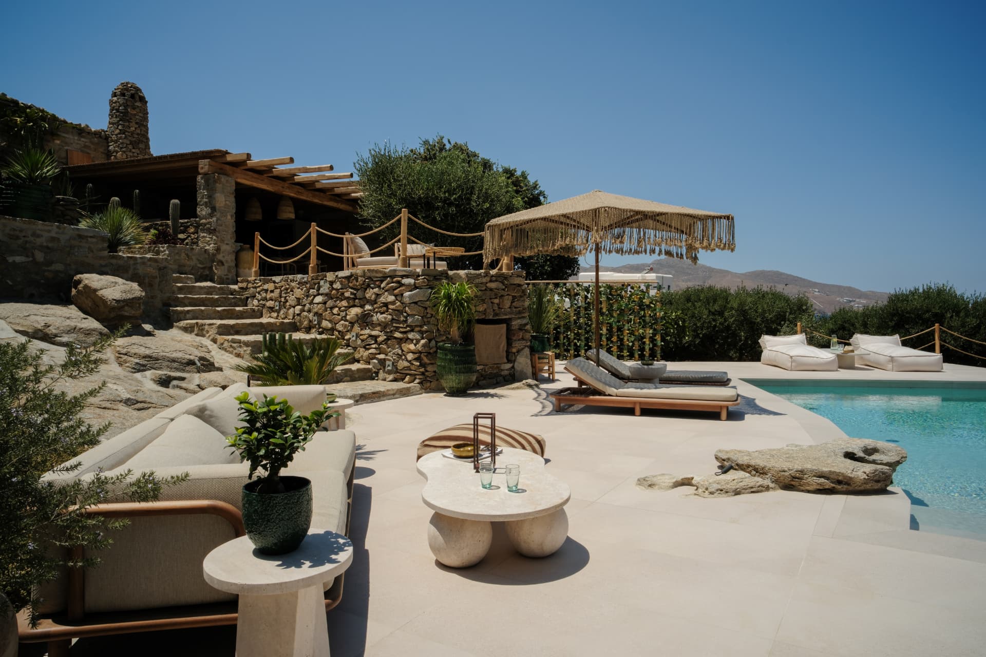 The outdoor living space by the pool — sofa, stone coffee table and sun loungers overlooking the hills