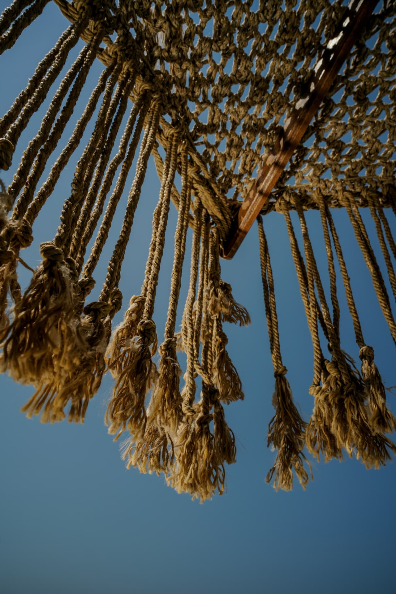 A woven fibre canopy with hanging tassels against the sky