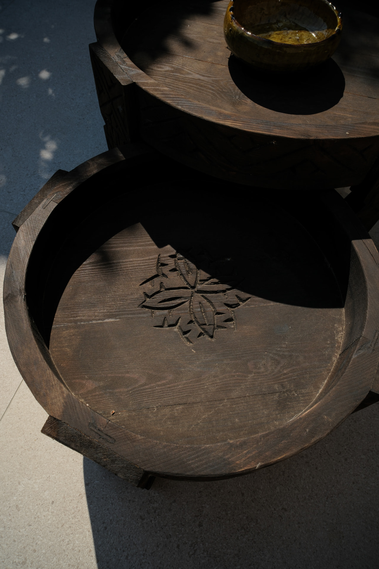 Two hand-carved dark wooden trays with floral patterns, a small olive-green glazed bowl resting on the top tray