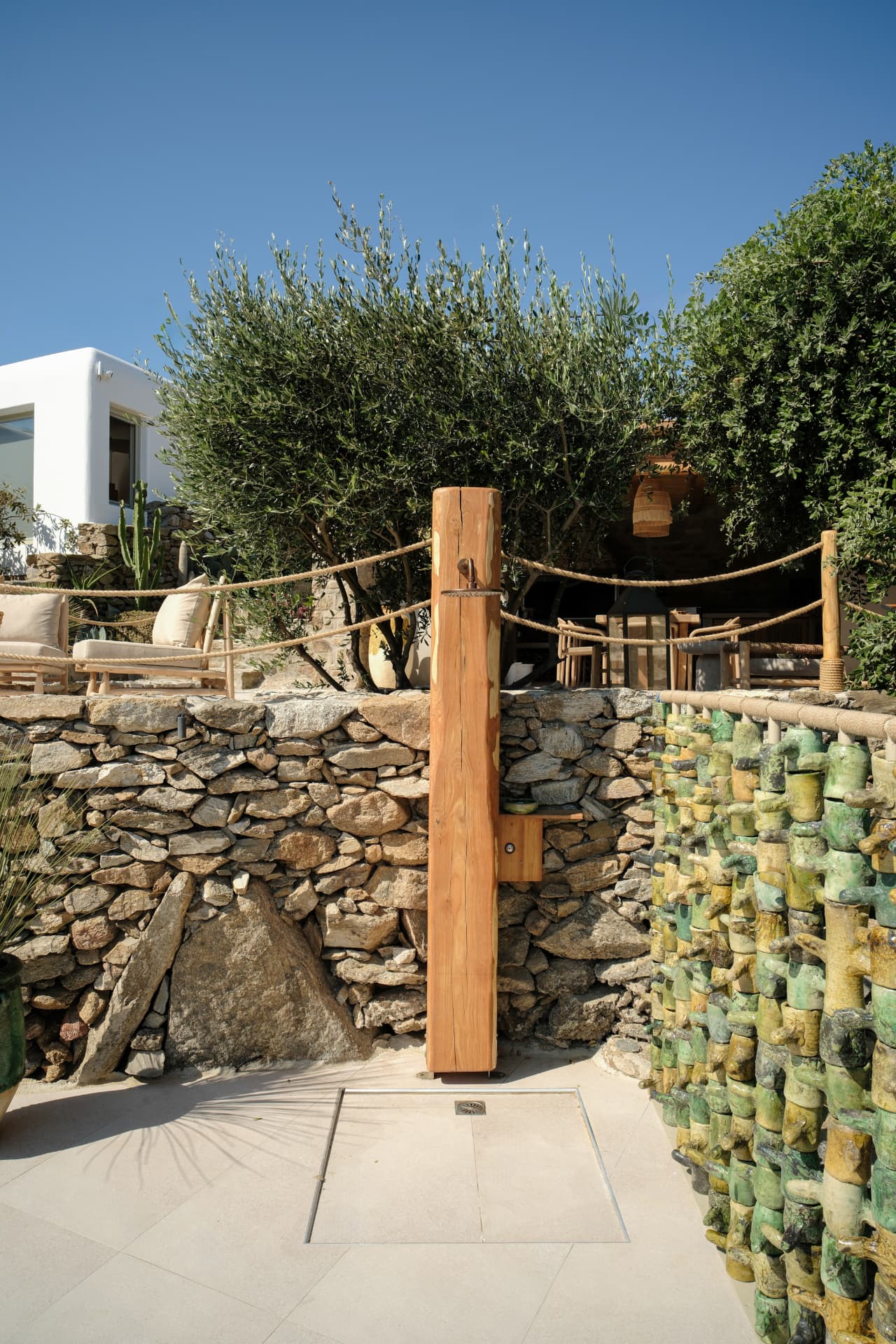 A minimalist outdoor shower on a natural wood post by the stone terrace