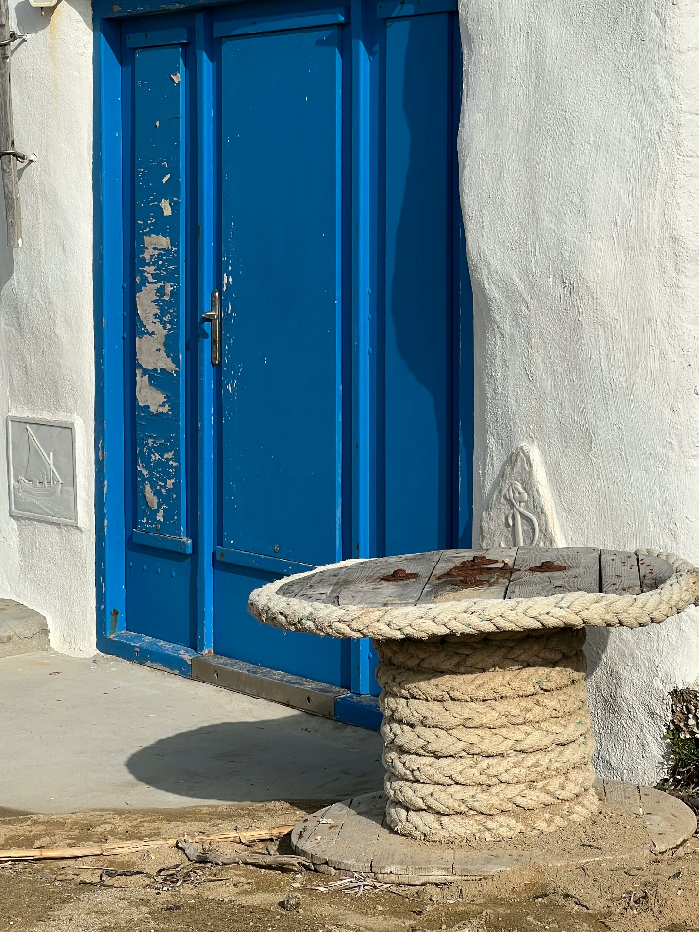 A weathered blue door and a rope-wrapped spool table, Ftelia, Mykonos