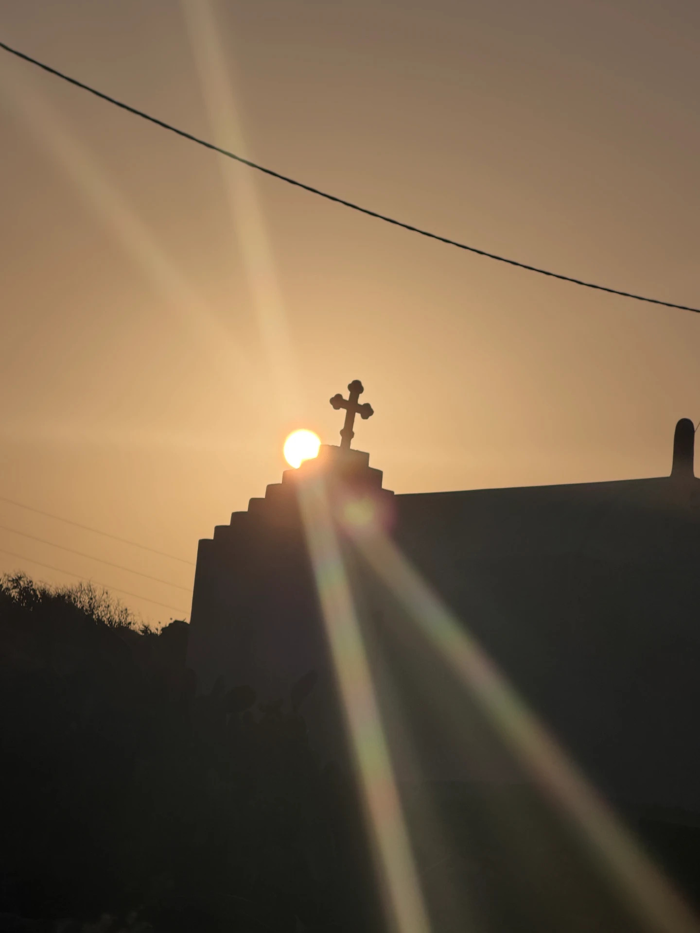 The silhouette of a small stone chapel back-lit by the setting sun