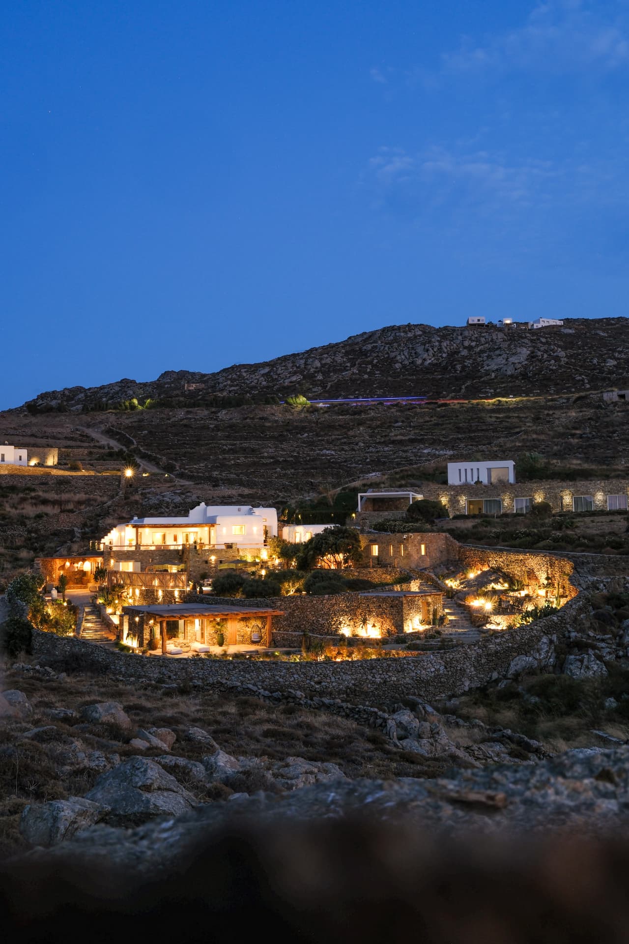 Twilight over Villa Storia: the multi-level hillside of white buildings and stone terraces glowing against a deep blue evening sky