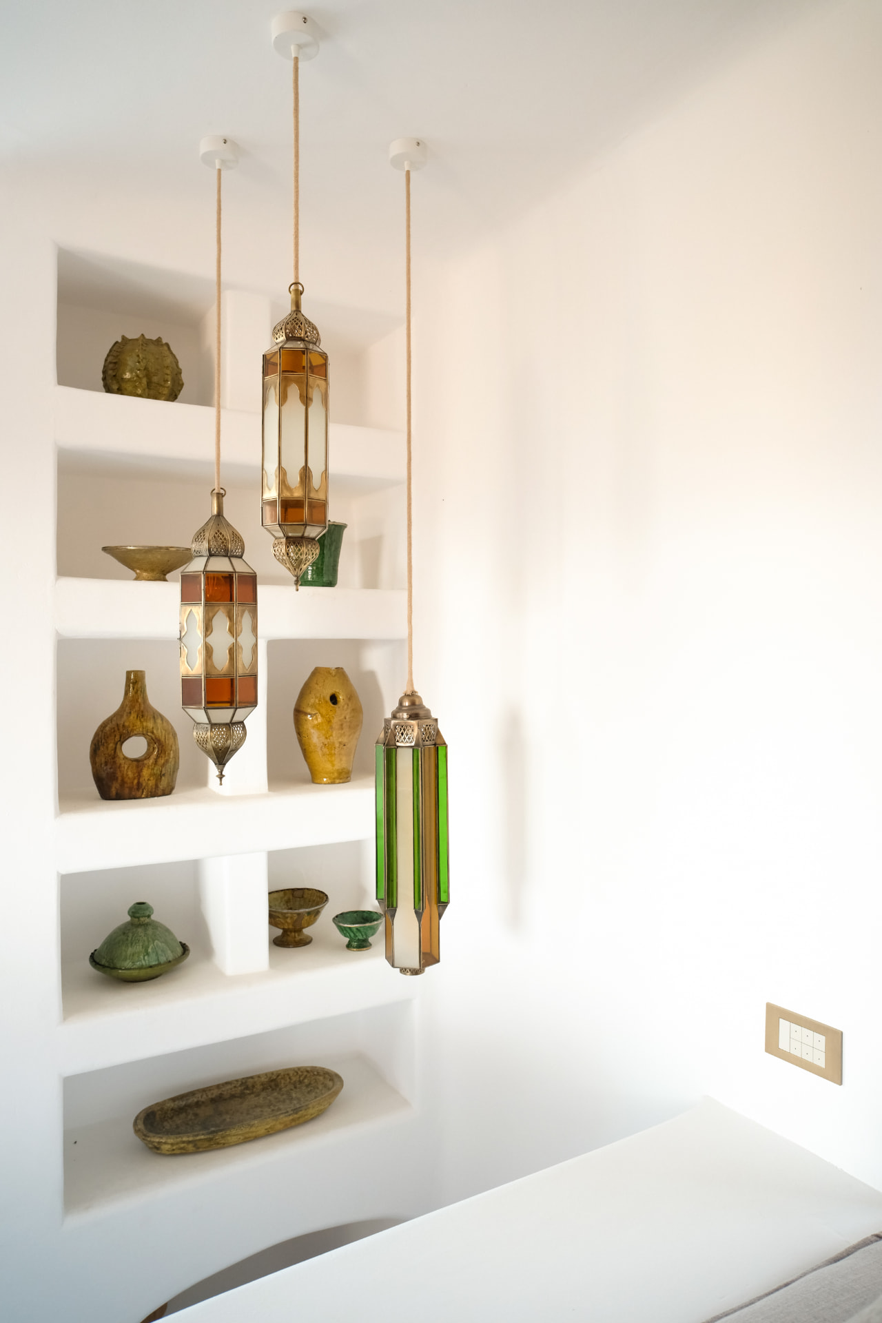 Detail, hanging amber and green stained-glass lanterns before ceramic niches